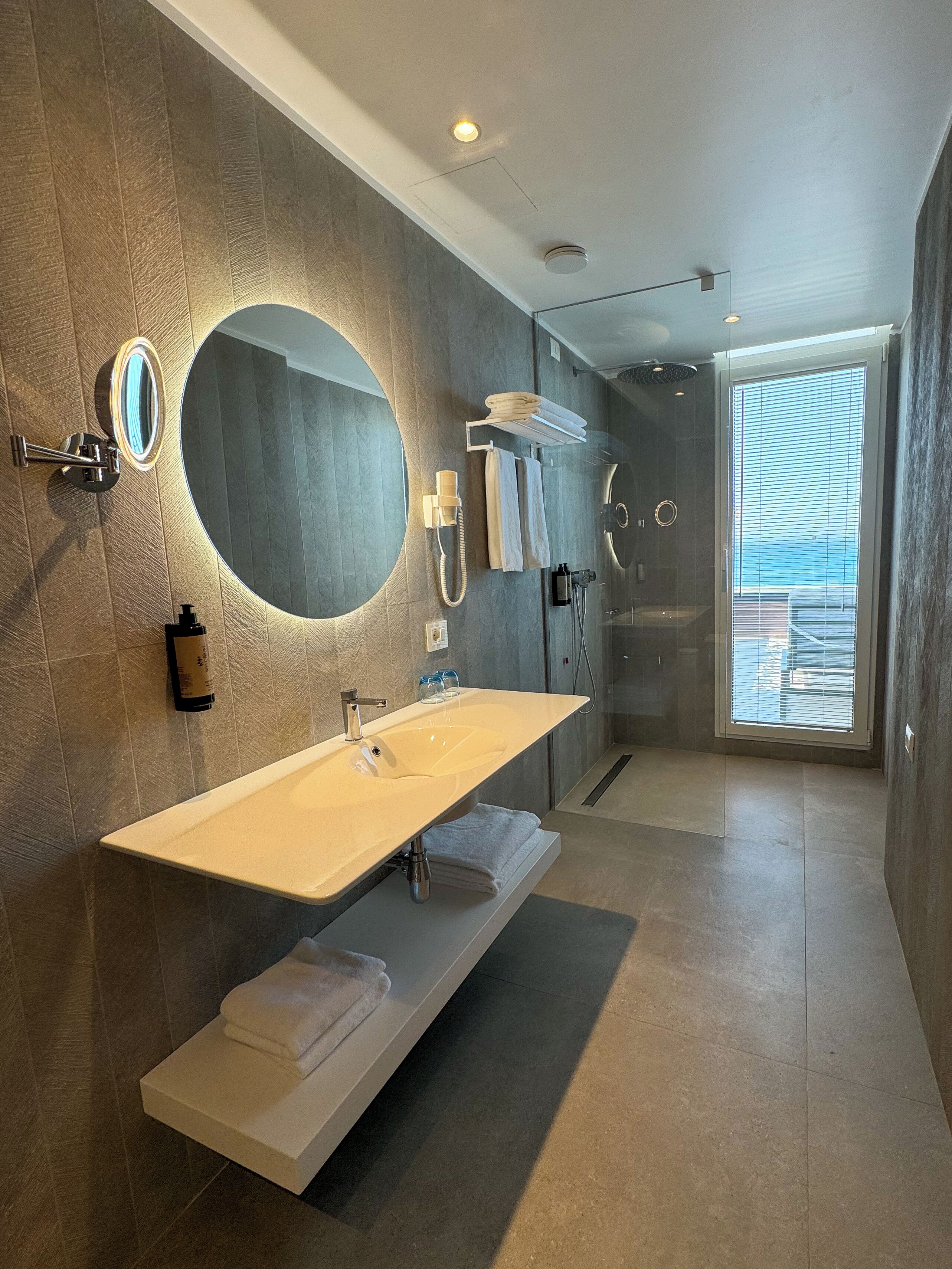 A modern bathroom with a large mirror, a vanity with a sink, a towel rack, and a shower area.