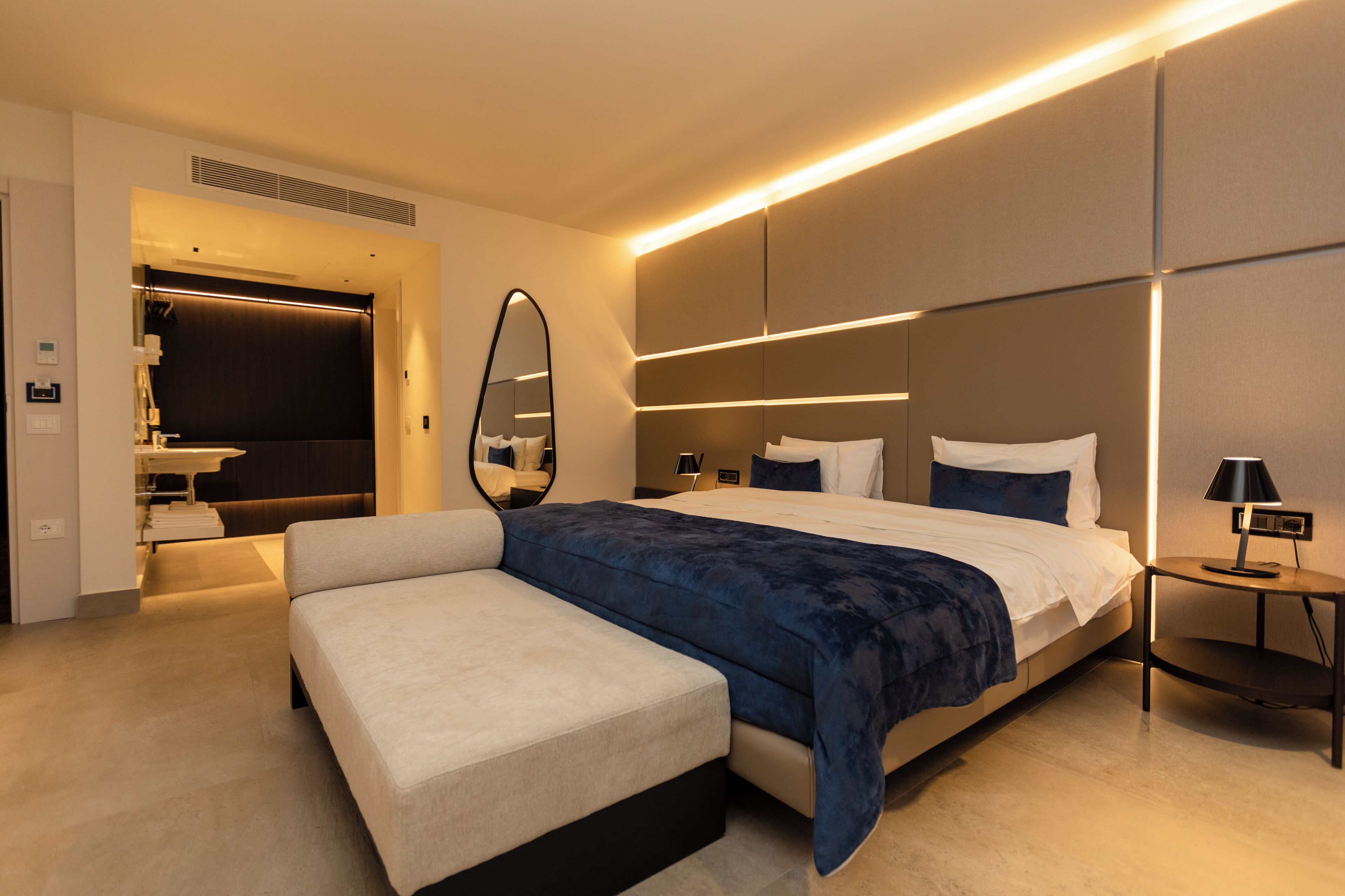 Una habitación de hotel moderna con una cama grande, mesitas de noche, un espejo y una zona de estar separada.