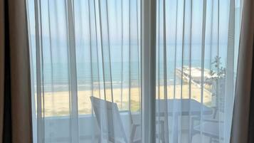 A room with a view of the beach through sheer curtains, a table, and chairs.