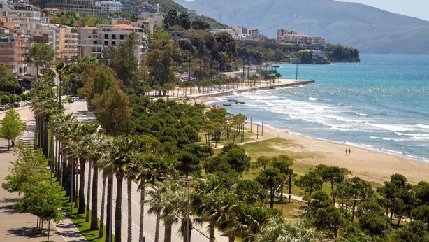 Un paysage urbain côtier avec une plage, des palmiers et des bâtiments le long de la côte.