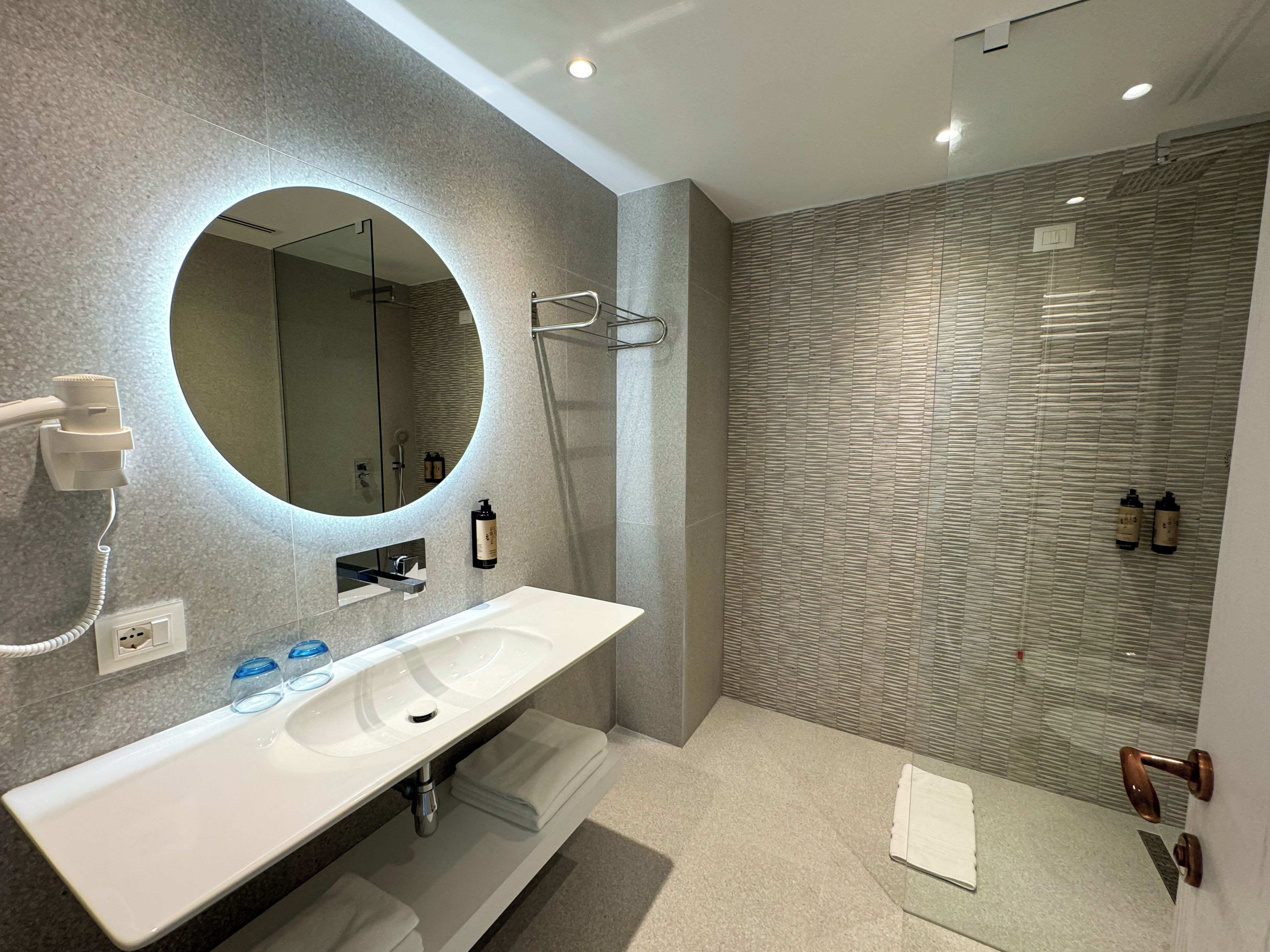 A modern bathroom with a large mirror, a white sink, and a shower area.