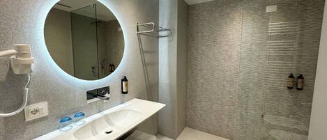 A modern bathroom with a large mirror, a white sink, and a shower area.