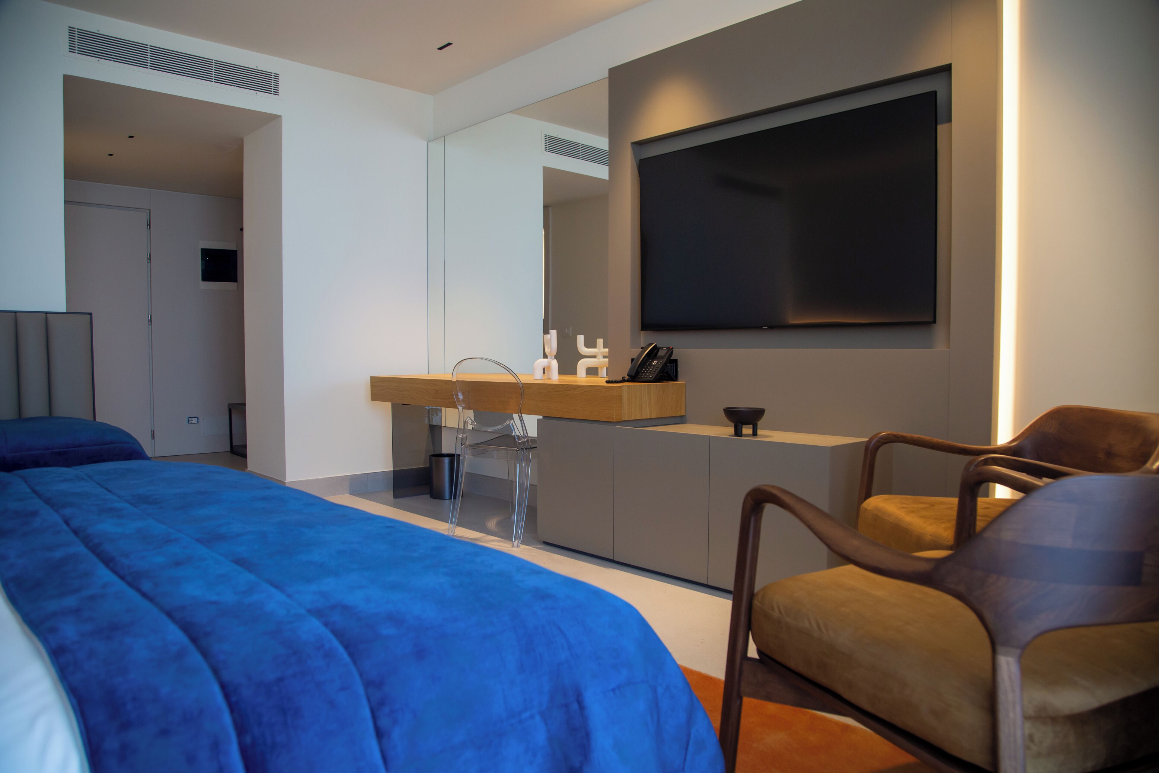 Un dormitorio moderno con una cama grande, un escritorio con una computadora, una silla y un televisor montado en la pared.