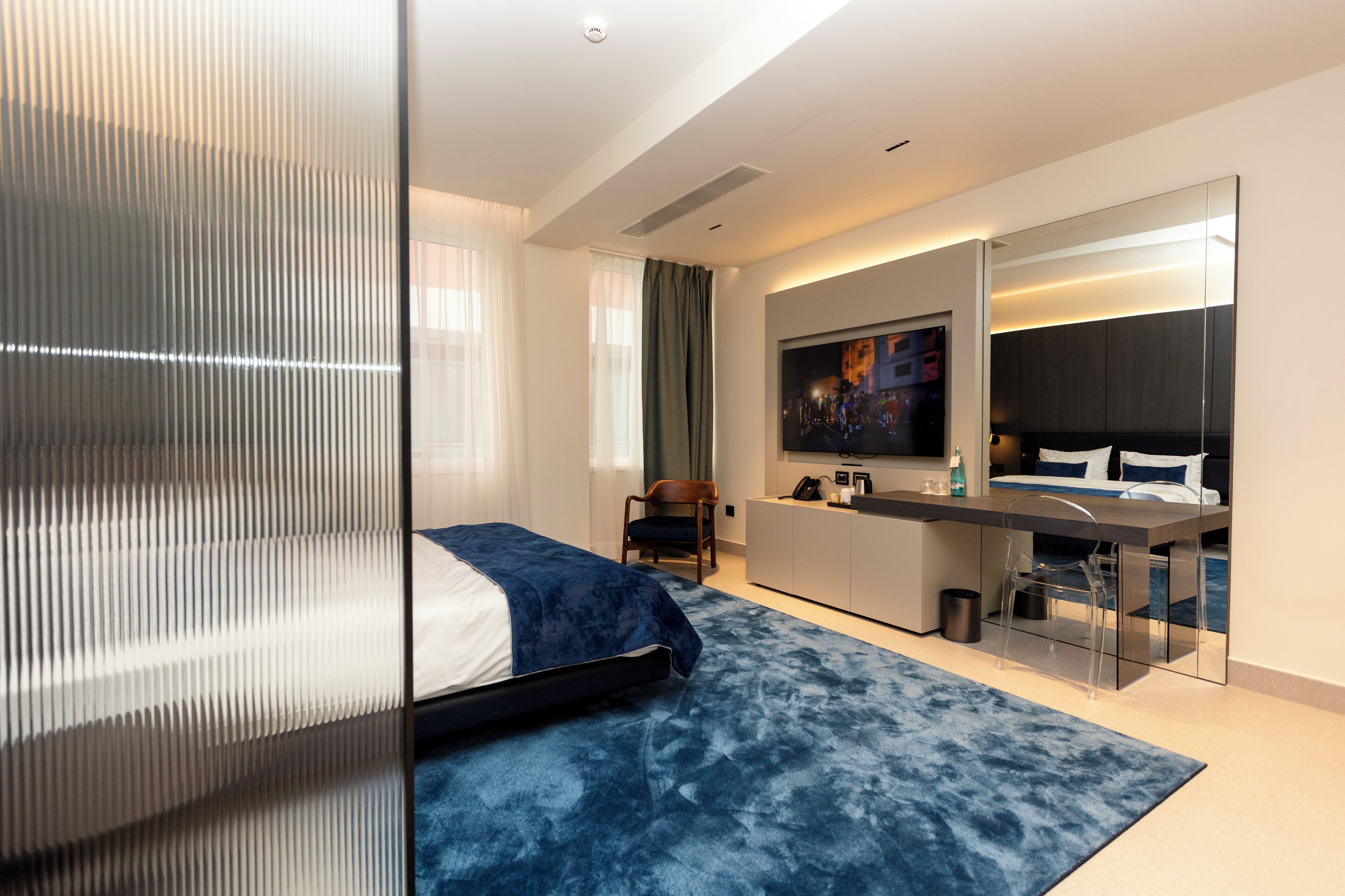 Une chambre d’hôtel moderne équipée d’un lit, d’un bureau, d’une chaise et d’un grand miroir.