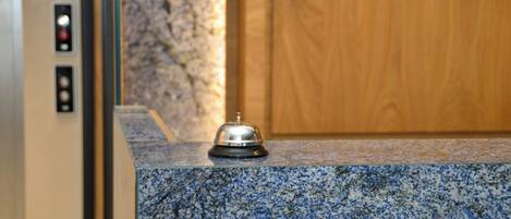 Una zona de recepción con mostrador de mármol, un timbre y una puerta de madera al fondo.