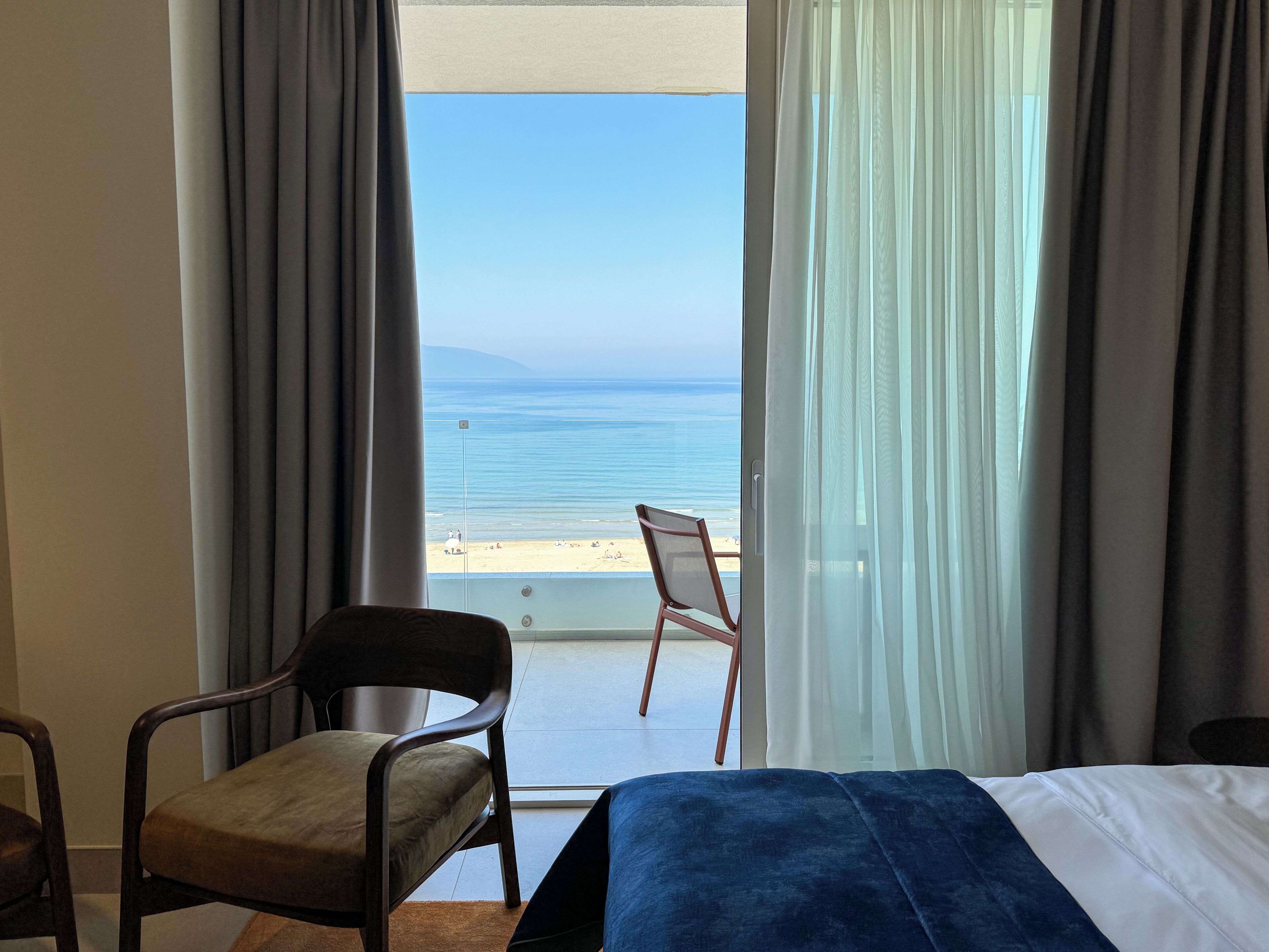 A hotel room with a bed, a chair, and a view of the beach and ocean.
