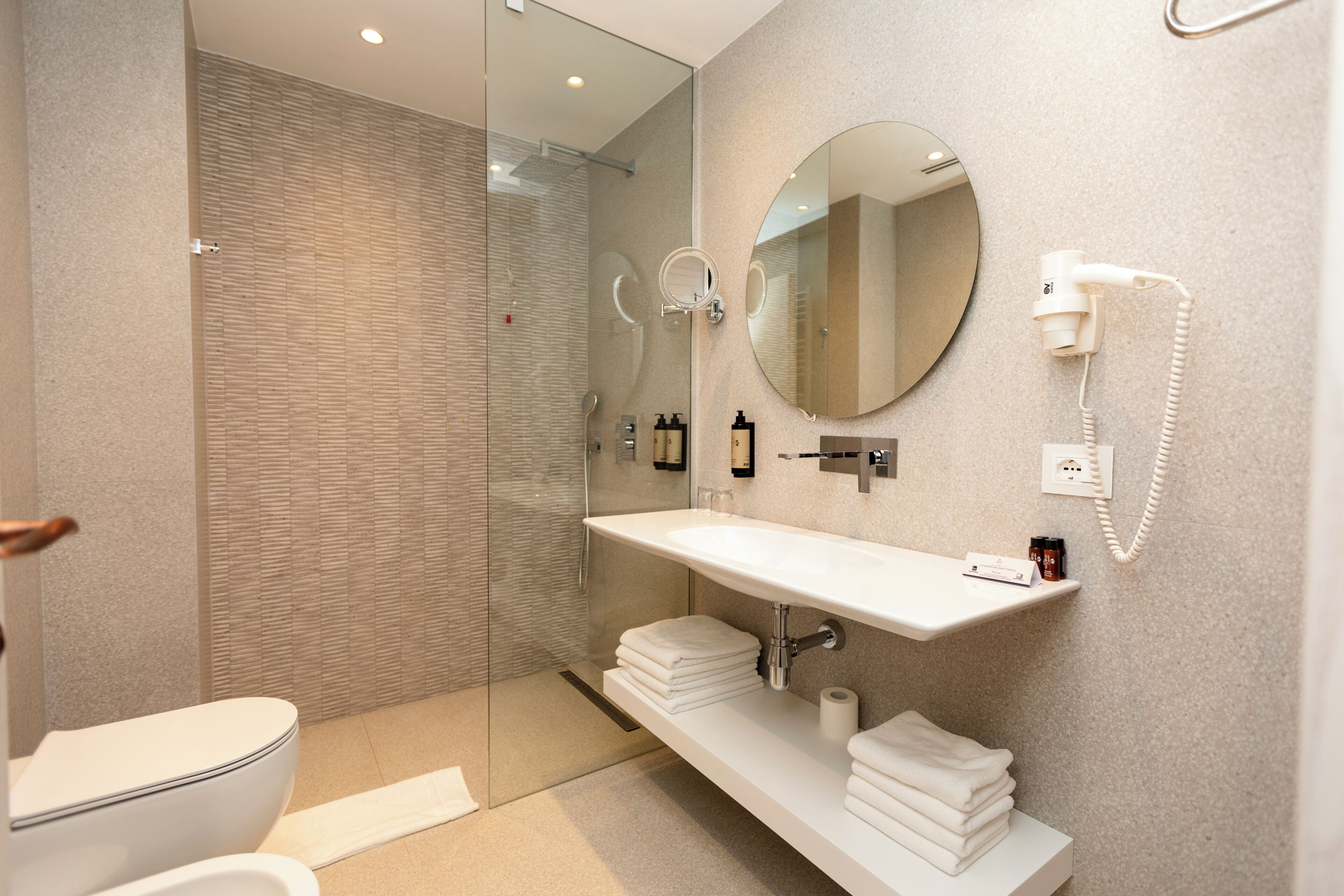 A modern bathroom with a glass shower enclosure, a white sink with a mirror above it, and a telephone mounted on the wall.