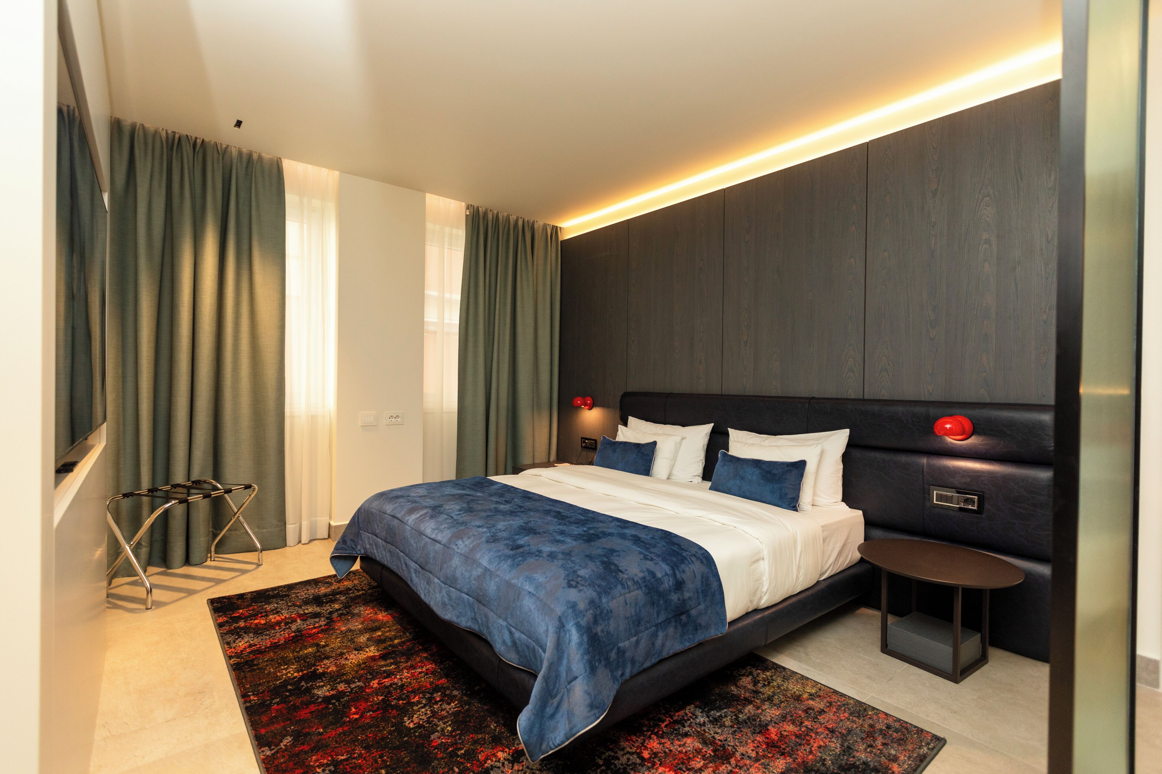A modern hotel room with a large bed, a bedside table, a nightstand, and a wall-mounted lamp.