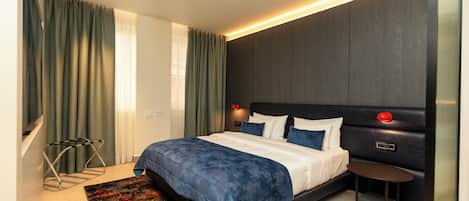 A modern hotel room with a large bed, a bedside table, a nightstand, and a wall-mounted lamp.