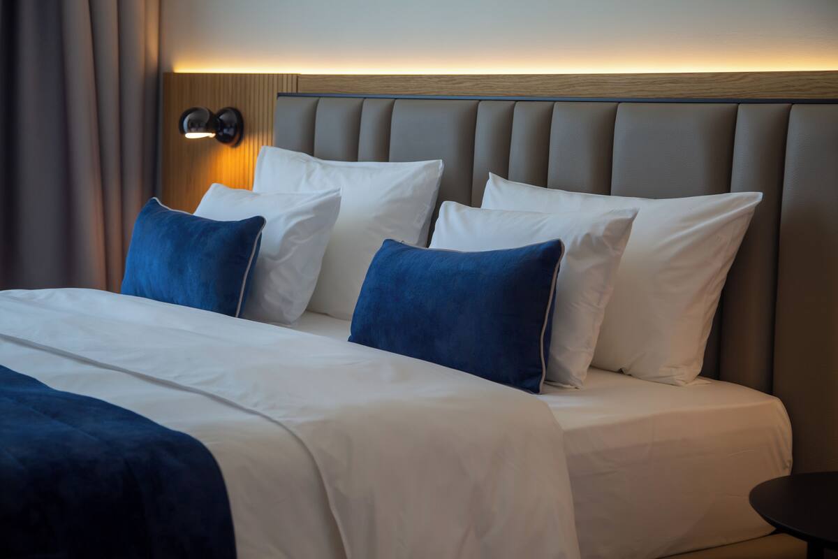 Ein Hotelzimmer mit einem großen Bett, vielen Kissen, einem Kopfteil mit Lichtleiste und einem kleinen Tisch.