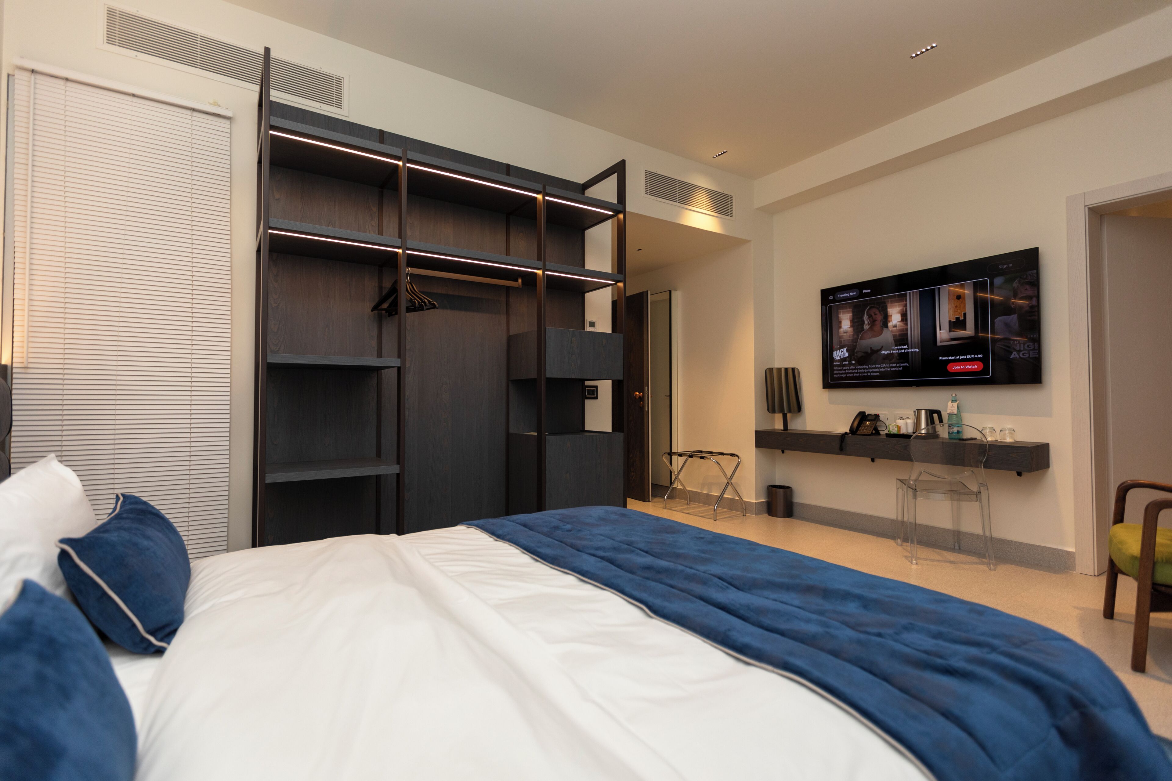 A bedroom with a bed, a wardrobe, a television, and a small table with a chair.