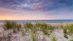A beach with sand and grass, and the ocean in the background.