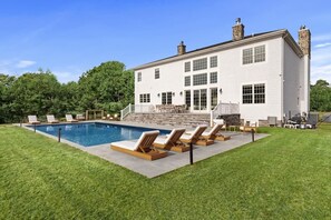 Une grande maison blanche avec une piscine, un espace salon extérieur et une cheminée en pierre.