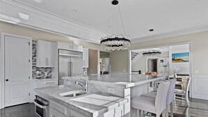 A modern kitchen with a large island, stainless steel appliances, and a chandelier.