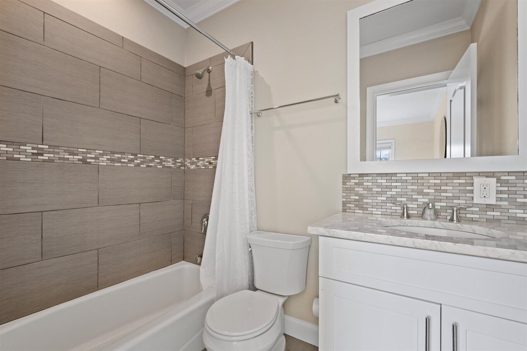 Baño con ducha, inodoro y lavamanos, con salpicadero de azulejos y espejo sobre el lavamanos.