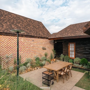 A patio with a wooden table and chairs, a brick wall, and a wooden cabin. - Pine Village (Mae On)