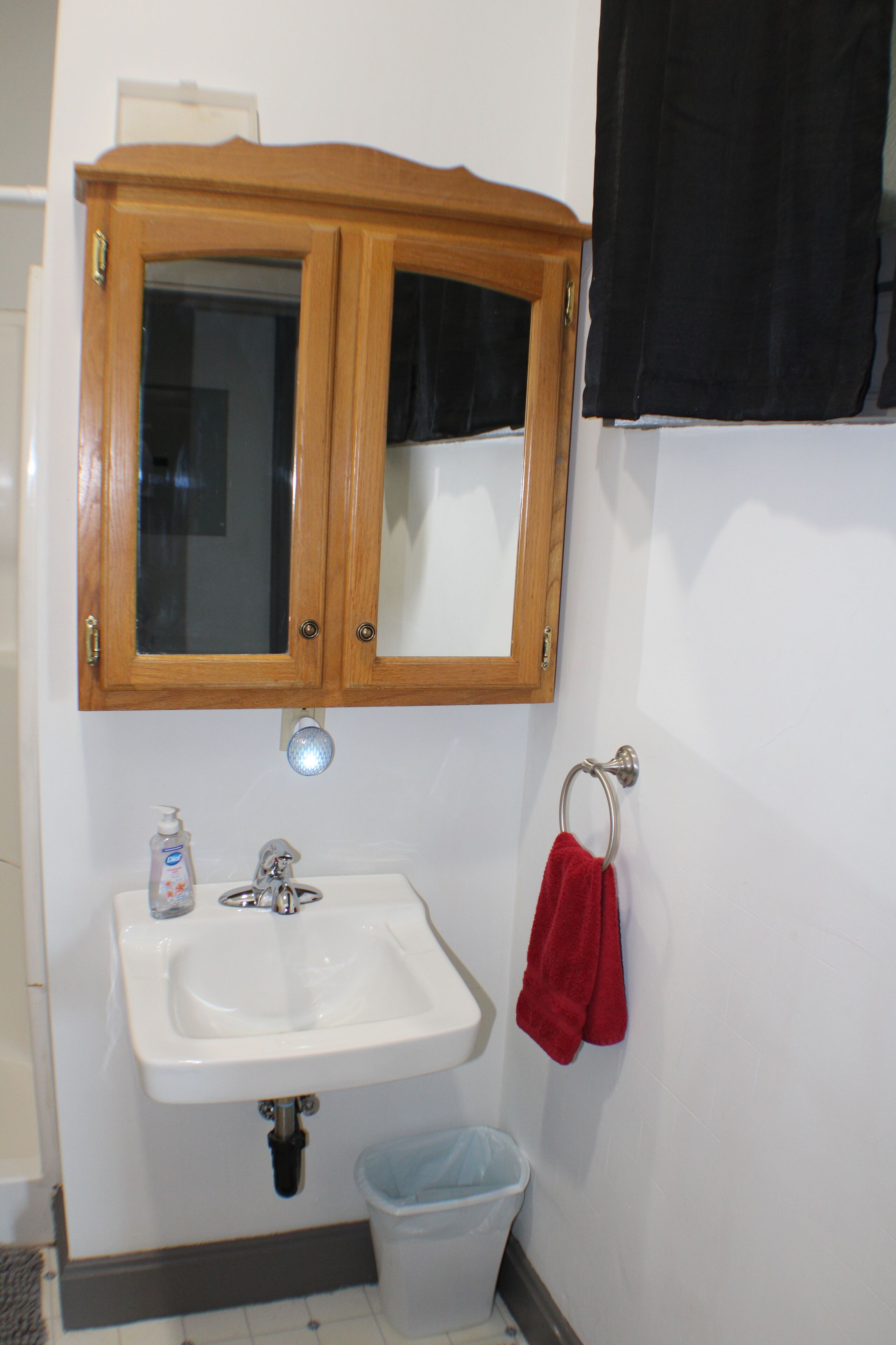 Een badkamer met een houten kastje, een wastafel, een spiegel, een rode handdoek en een prullenbak.