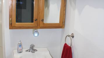 Een badkamer met een houten kastje, een wastafel, een spiegel, een rode handdoek en een prullenbak.