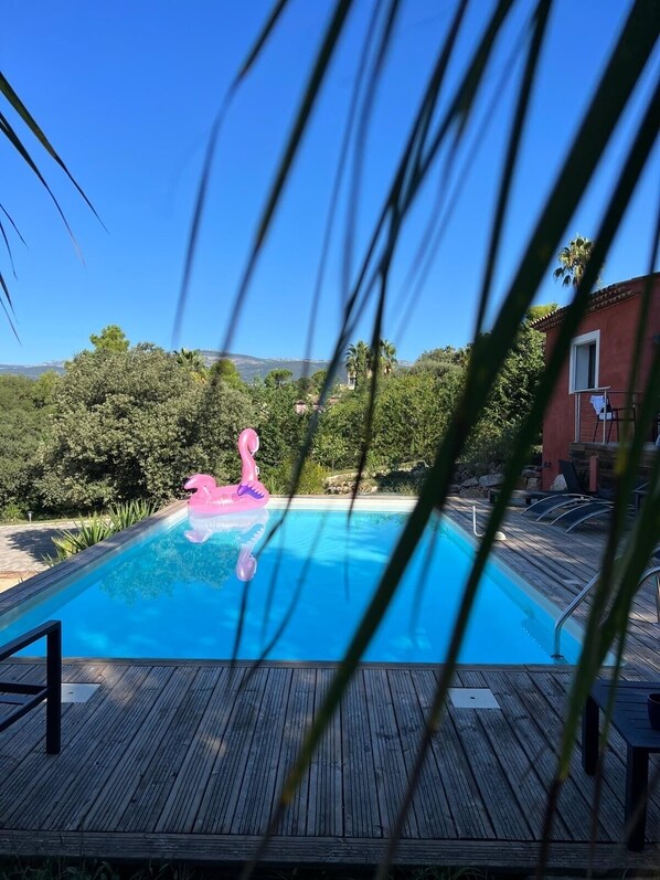 A swimming pool with a wooden deck, surrounded by greenery and a clear sky. - Villa Avec Piscine AU Calme EN Pleine Nature (Mouans-Sartoux)