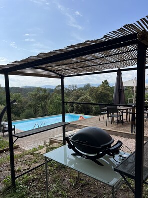A covered outdoor area with a barbecue grill, pool, and dining table with chairs. - Villa Avec Piscine AU Calme EN Pleine Nature (Mouans-Sartoux)