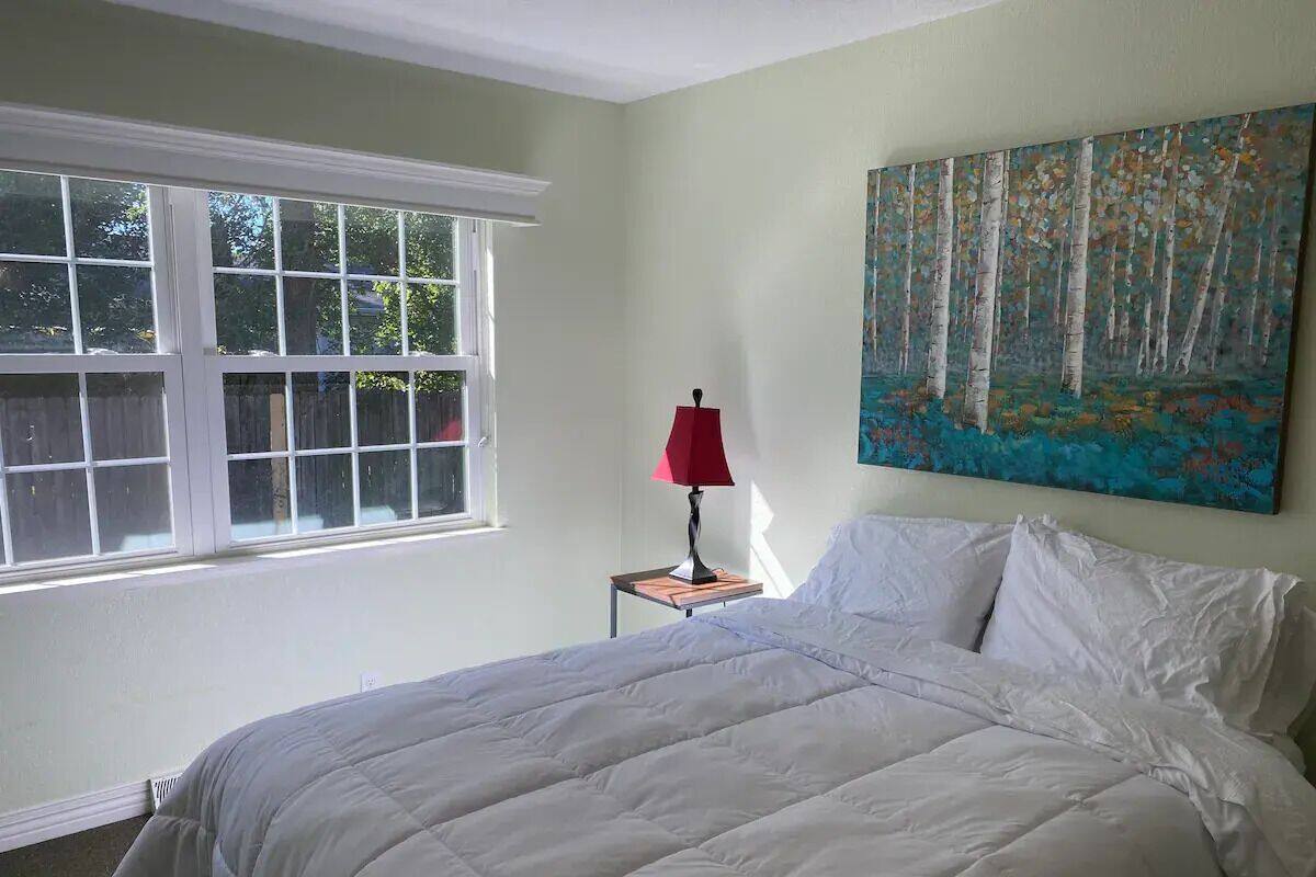 Ein Schlafzimmer mit einem Bett, einem Fenster, einem Nachttisch mit Lampe und einem Bild an der Wand.