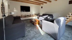 Una sala moderna con un televisor de pantalla plana en la pared, vigas de madera en el techo y un sofá con sillones.