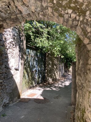 A narrow stone pathway flanked by walls with greenery and a metal gate. - House on the river (Ganges)