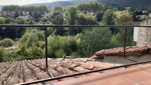 Une terrasse dallée de carreaux de terre cuite et dotée d’une rambarde en métal, qui offre une vue sur un village avec ses maisons et ses arbres.