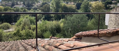 A terrace with terracotta tiles and a metal railing, overlooking a village with houses and trees.