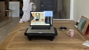 Un ordinateur portable est posé sur un bureau en bois dans une pièce où se trouvent un escalier et une porte donnant sur l’extérieur.