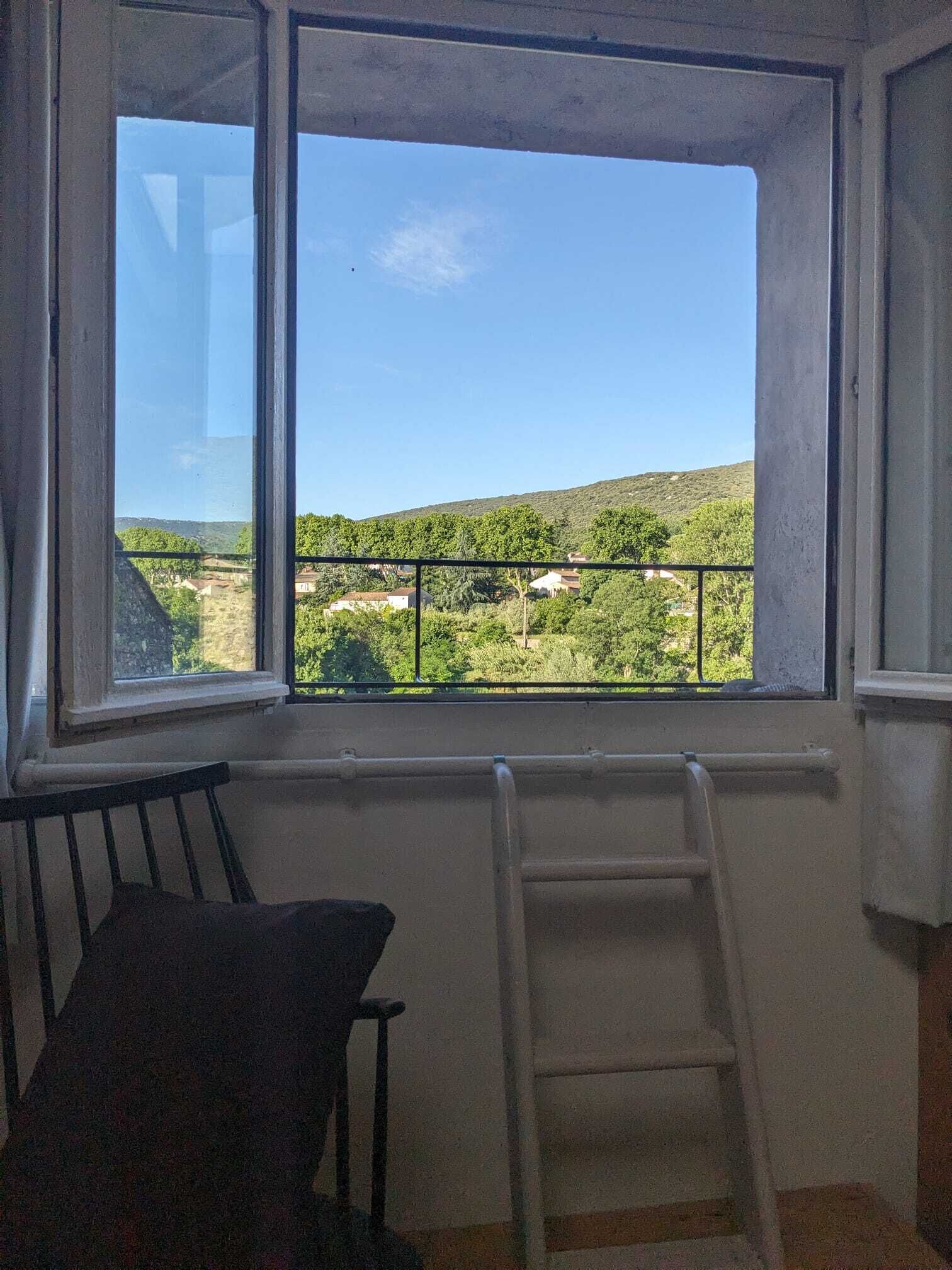 A room with a large window offering a view of a green landscape and hills.