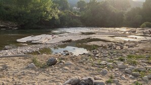 Une rive de rivière bordée de rochers et de galets, entourée de verdure.