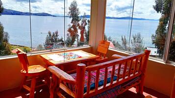 A wooden table with a painting, a chair, and a view of a lake through large windows.