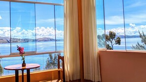 Una habitación con cama, una mesita de noche con un florero y vistas a un lago y montañas.