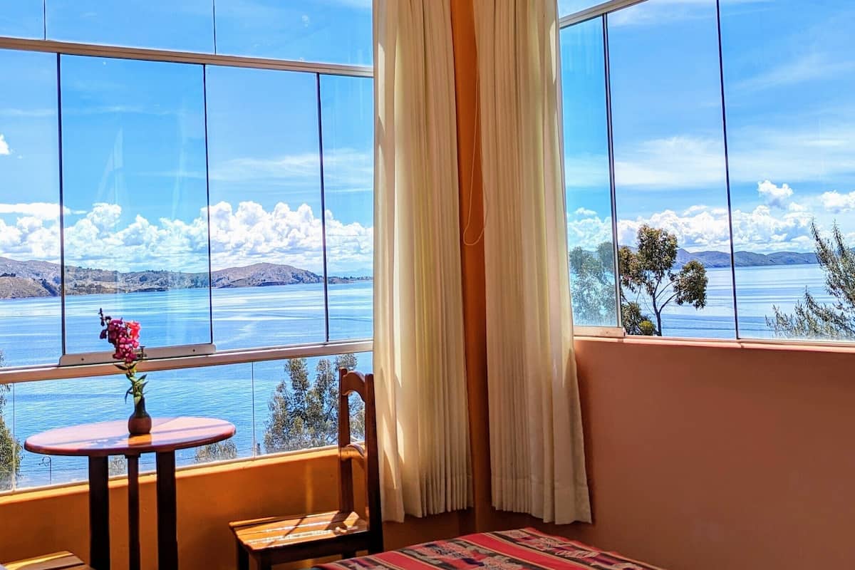Une chambre avec un lit, une petite table sur laquelle est posé un vase, et une vue sur un lac et des montagnes.