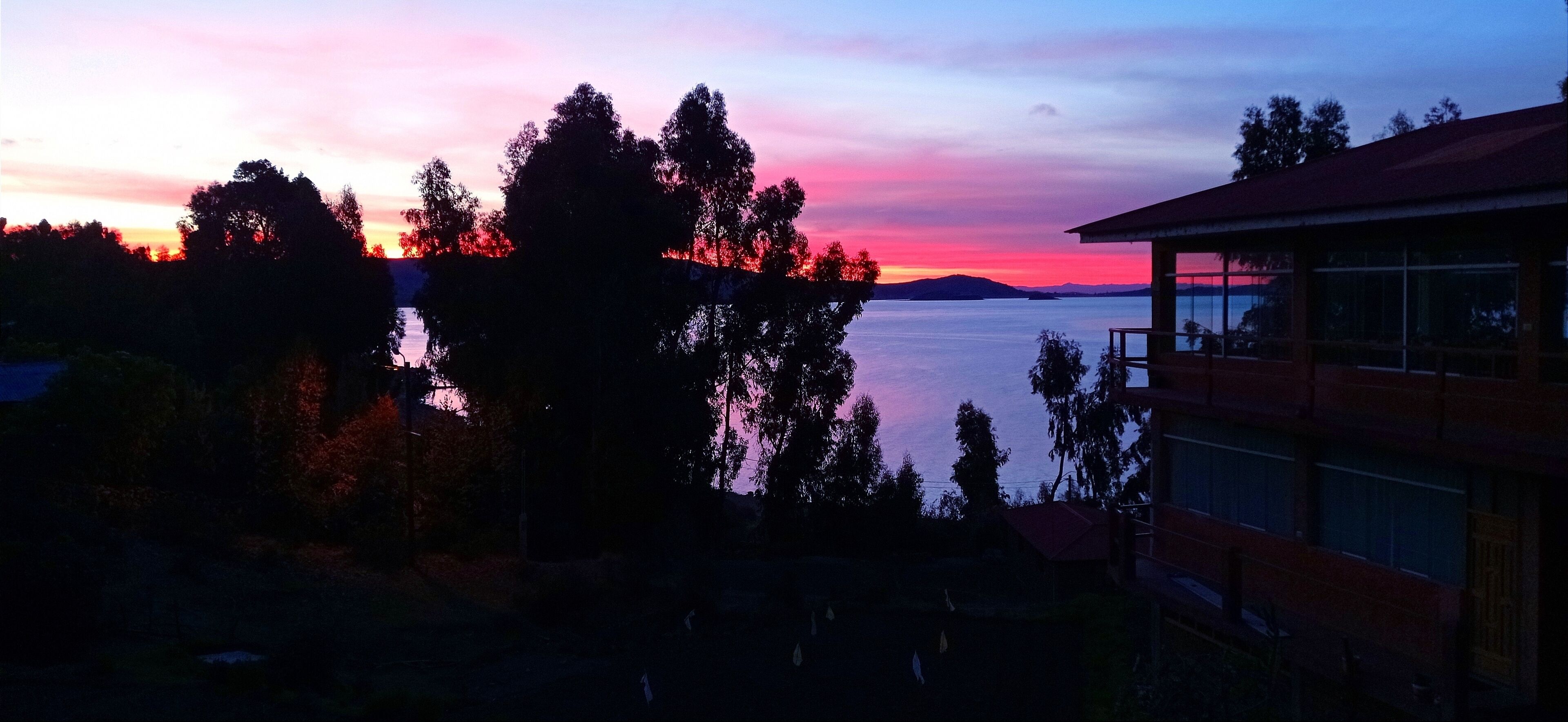 A building with a balcony overlooking a body of water and trees during sunset.