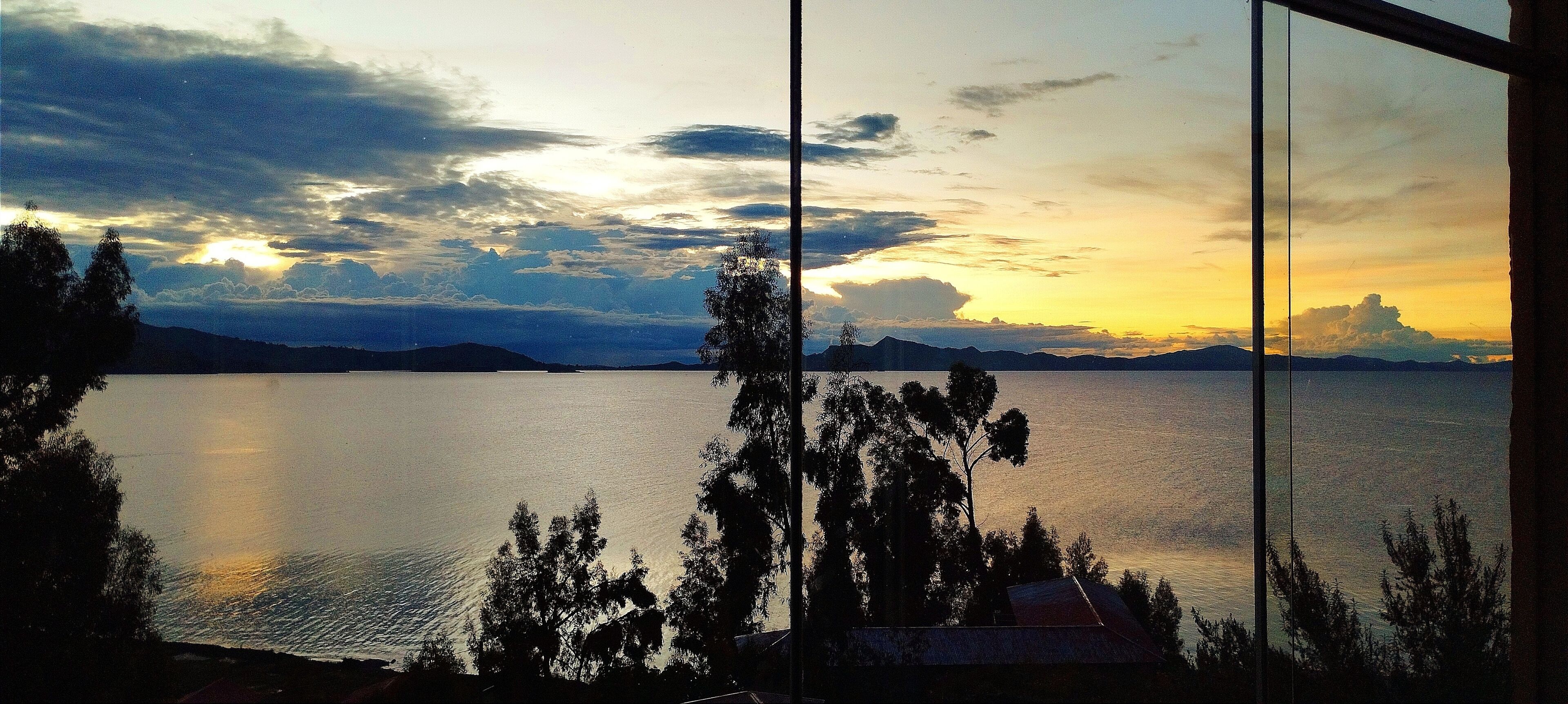 Une vue sur un lac, avec des montagnes à l'horizon, telle qu'elle apparaît à travers une fenêtre équipée de stores verticaux.