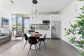 Uma cozinha moderna com armários brancos, uma área de refeições com mesa e cadeiras redondas, e uma janela grande com vista para o exterior.