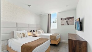 A hotel room with two beds, a wooden nightstand, a flat-screen TV, and a window with a cityscape view. - South Beach Oasis, 2-Bed Elegant Gem (Miami Beach)