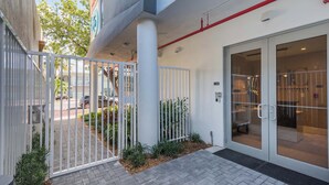 A gated entrance with a metal fence, a paved walkway, and a building entrance with glass doors. - South Beach Oasis, 2-Bed Elegant Gem (Miami Beach)