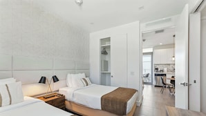 A modern hotel room with a large bed, a bedside table with lamps, a wardrobe, and a view into the kitchen area. - Elegant SoBe 2 Bedroom Apartment (Miami Beach)