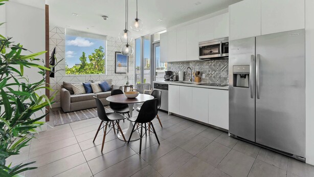 A modern kitchen with a dining area, stainless steel appliances, and a view of greenery. - Elegant SoBe 2 Bedroom Apartment (Miami Beach)