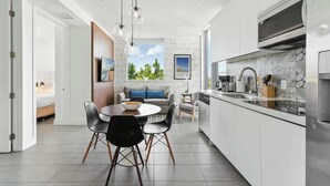A modern kitchen with a dining area, large windows, and a view of greenery. - Elegant SoBe 2 Bedroom Apartment (Miami Beach)