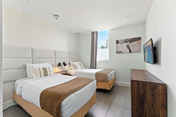 A hotel room with two beds, a wooden nightstand, a flat-screen TV, and a window with a cityscape view.