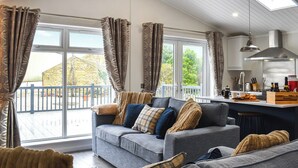 Ein modernes Wohnzimmer mit grauem Sofagarnitur, einem Holztisch und Blick auf ein Steingebäude.