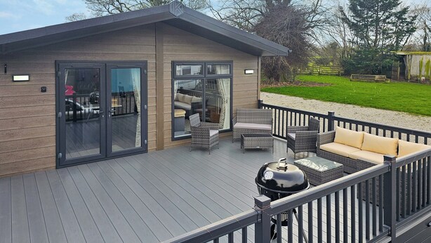 Eine moderne Außenterrasse mit Grill, Korbmöbeln und einer Glastür, die zu einem Innenbereich führt.