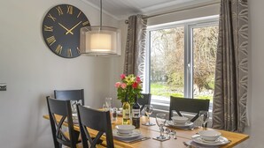 Ein Essbereich mit einem Holztisch, schwarzen Stühlen, einer Wanduhr und einem Fenster mit Vorhängen.