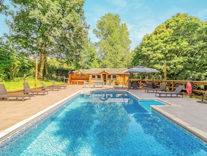 A swimming pool with lounge chairs, a wooden cabin, and surrounding greenery.