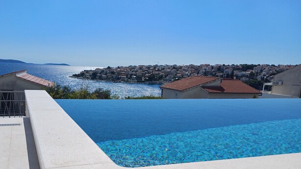 Una piscina con agua azul cristalina, rodeada de edificios y vista al mar.