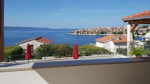 Una terraza con sombrillas rojas, vista al mar y un pueblo costero de fondo.